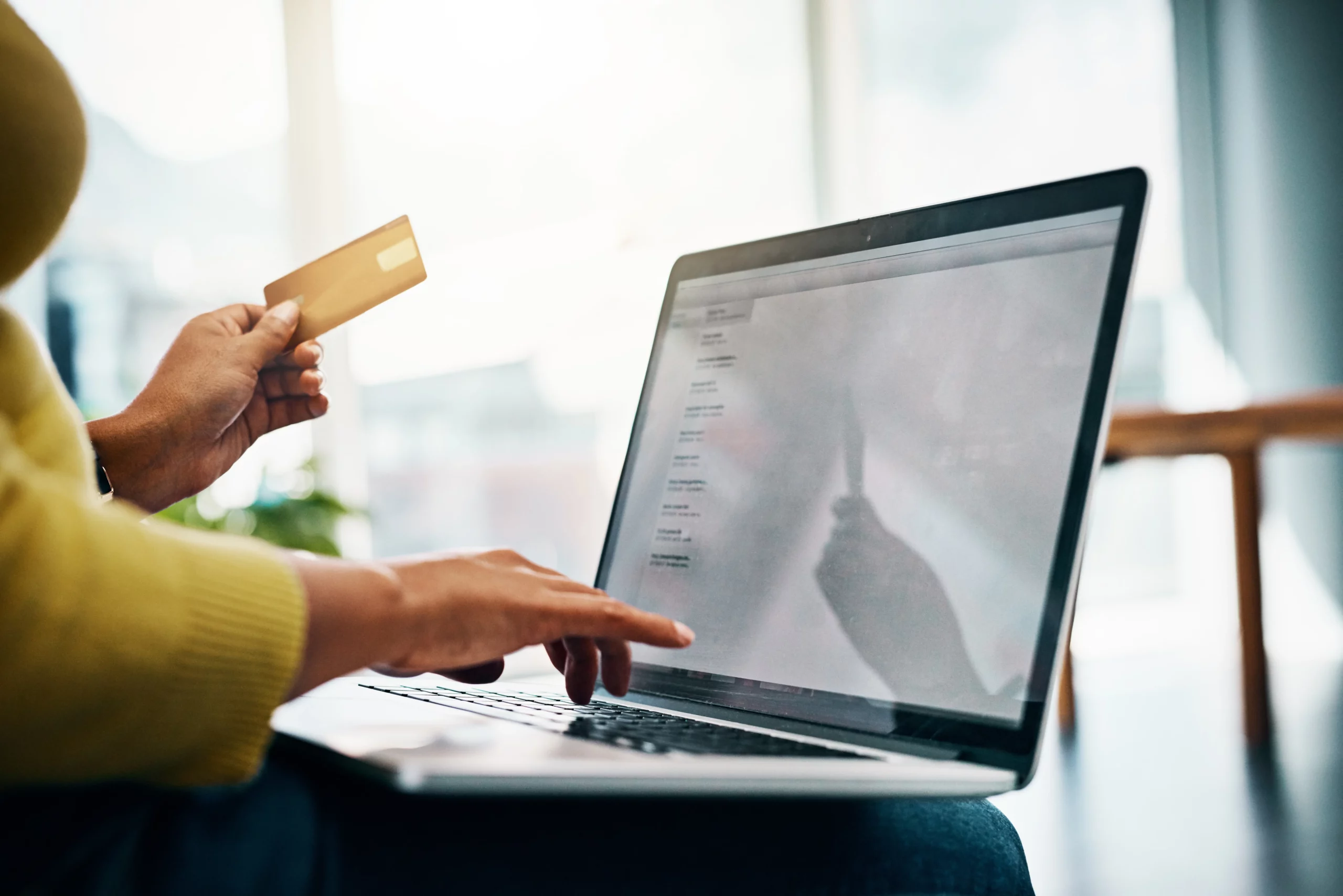 Person holds a credit card while working on a laptop in sunlit room, symbolizing rebuilding credit after bankruptcy through responsible use and planning.