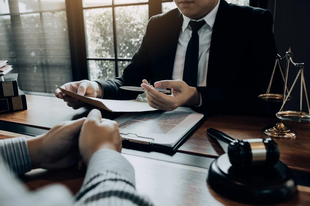 Lawyer in a suit reviews documents with a client at a wooden desk, with gavel and justice scales present—representing Chapter 7 bankruptcy consultation.