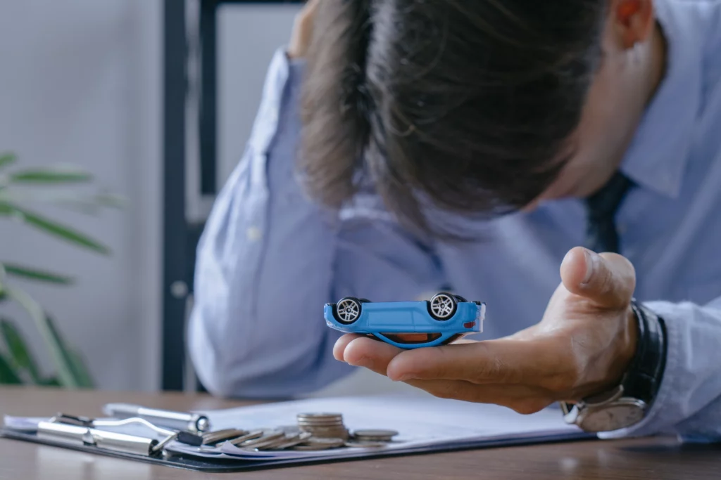 Stressed individual in business attire holding a toy car upside down while sitting at a desk with documents and coins, representing financial difficulty and concerns about keeping a vehicle during bankruptcy in Santa Rosa, California.